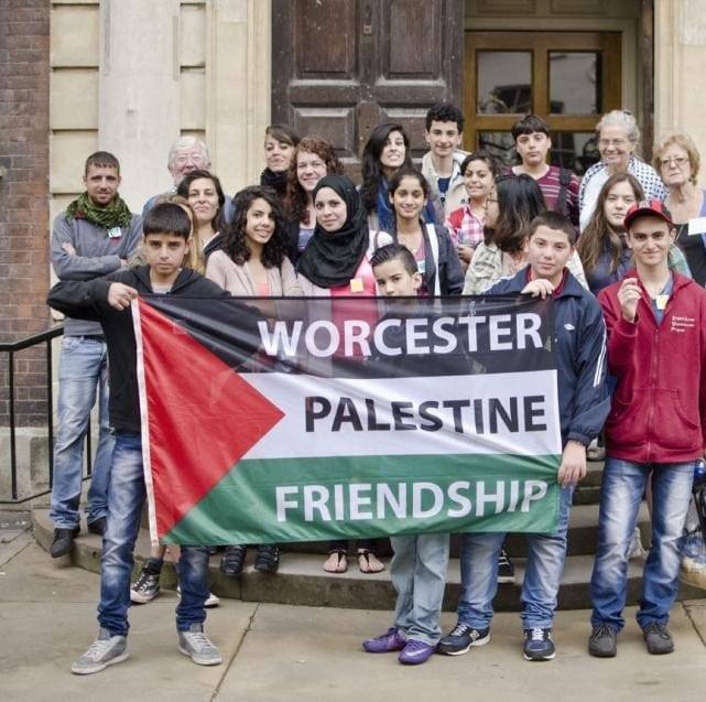 A group of people holding a Palestinian flag with the words Worcester Palestine Friendship